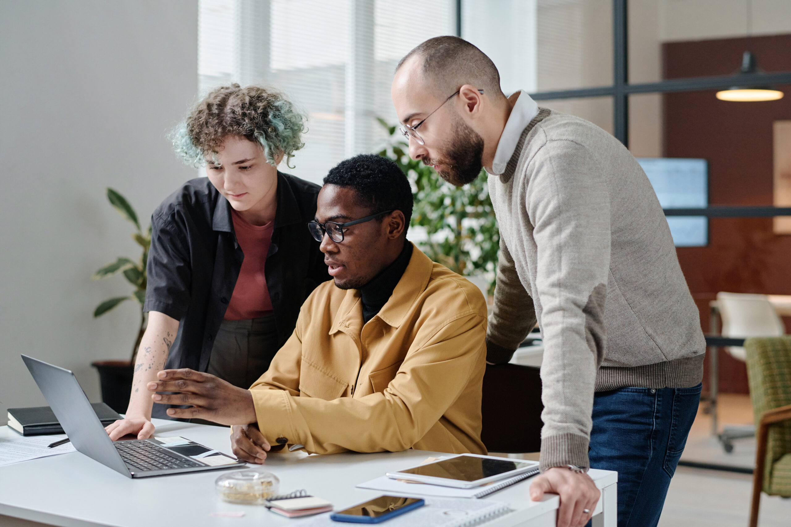 Young office workers examining information of laptop, black man talking to his colleagues